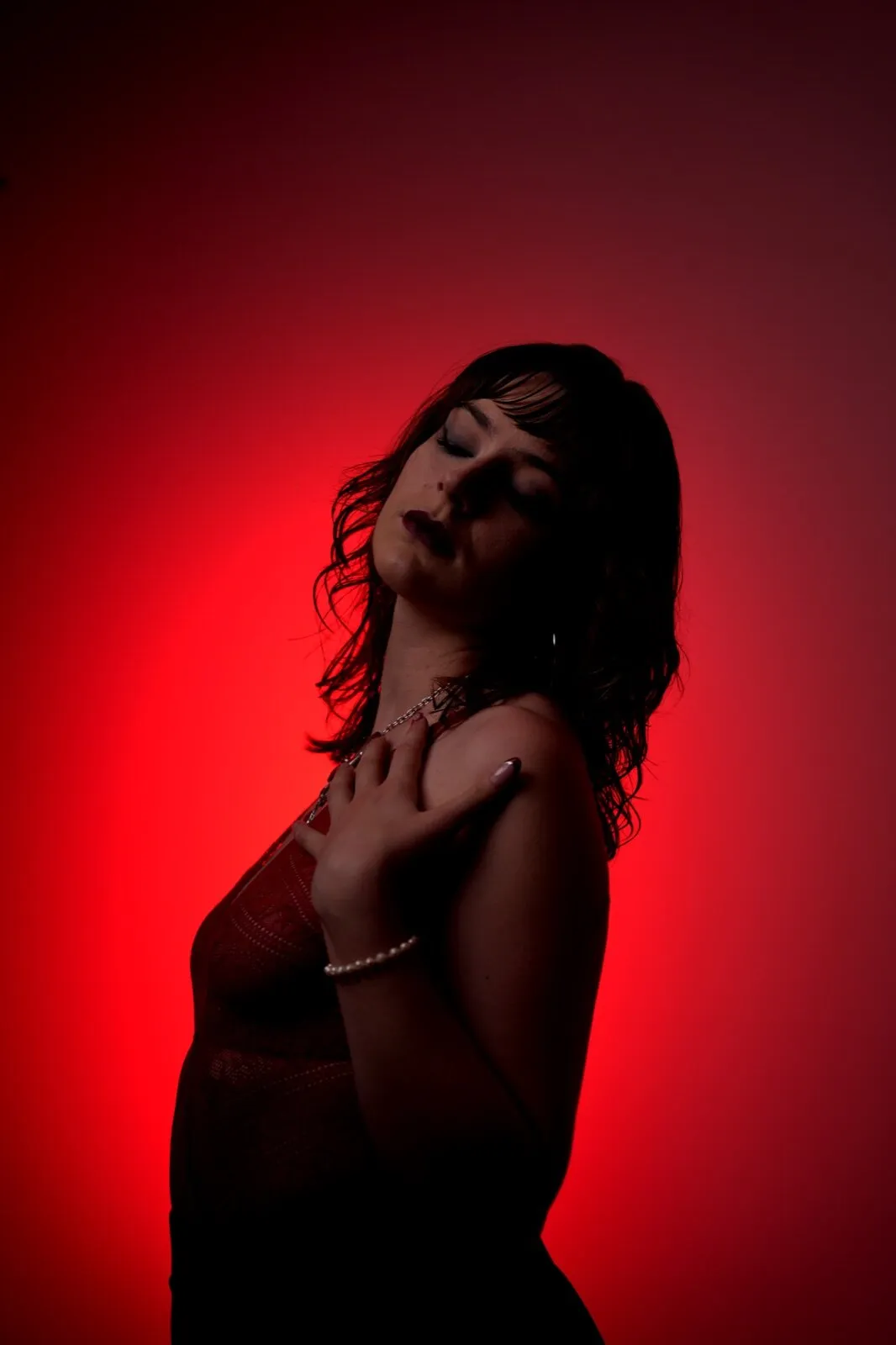 Pose cambrée en clair-obscur rouge, collier de perles